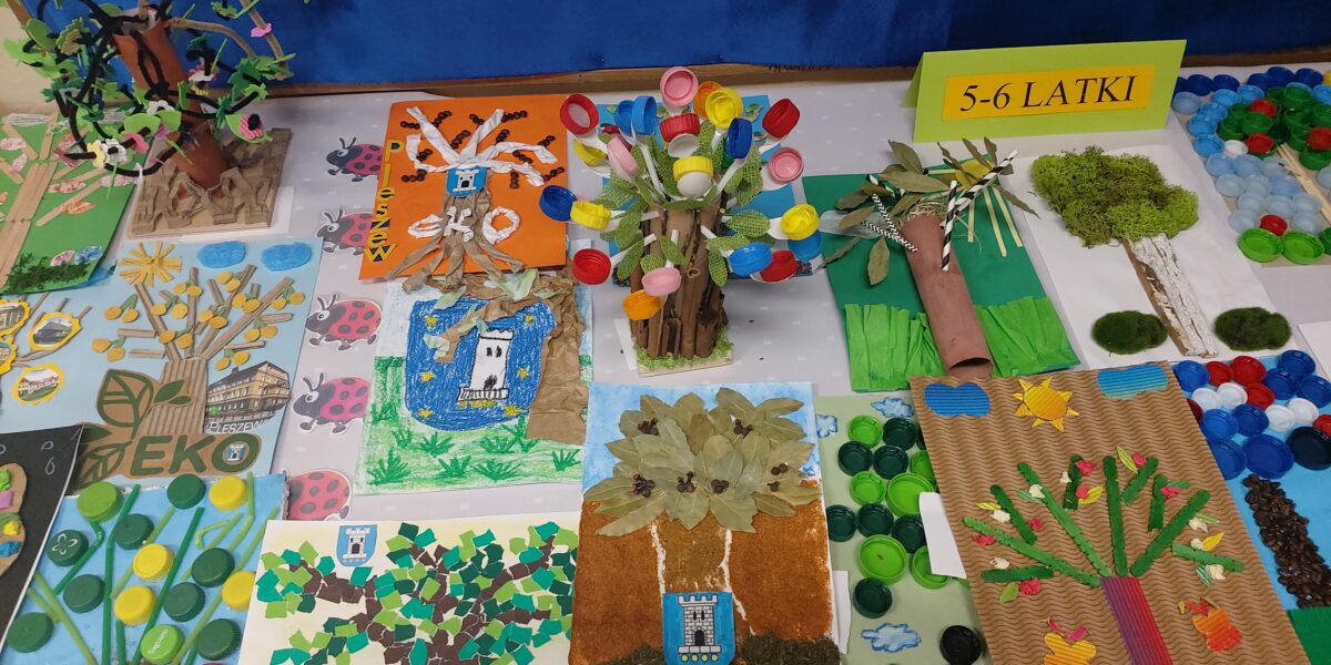 prace plastyczne dzieci rozłozone na stoliku, przedstawiające drzewo, wykonane różnymi technikami plastycznymi, dominuje kolor zielony, brązowy i niebieski